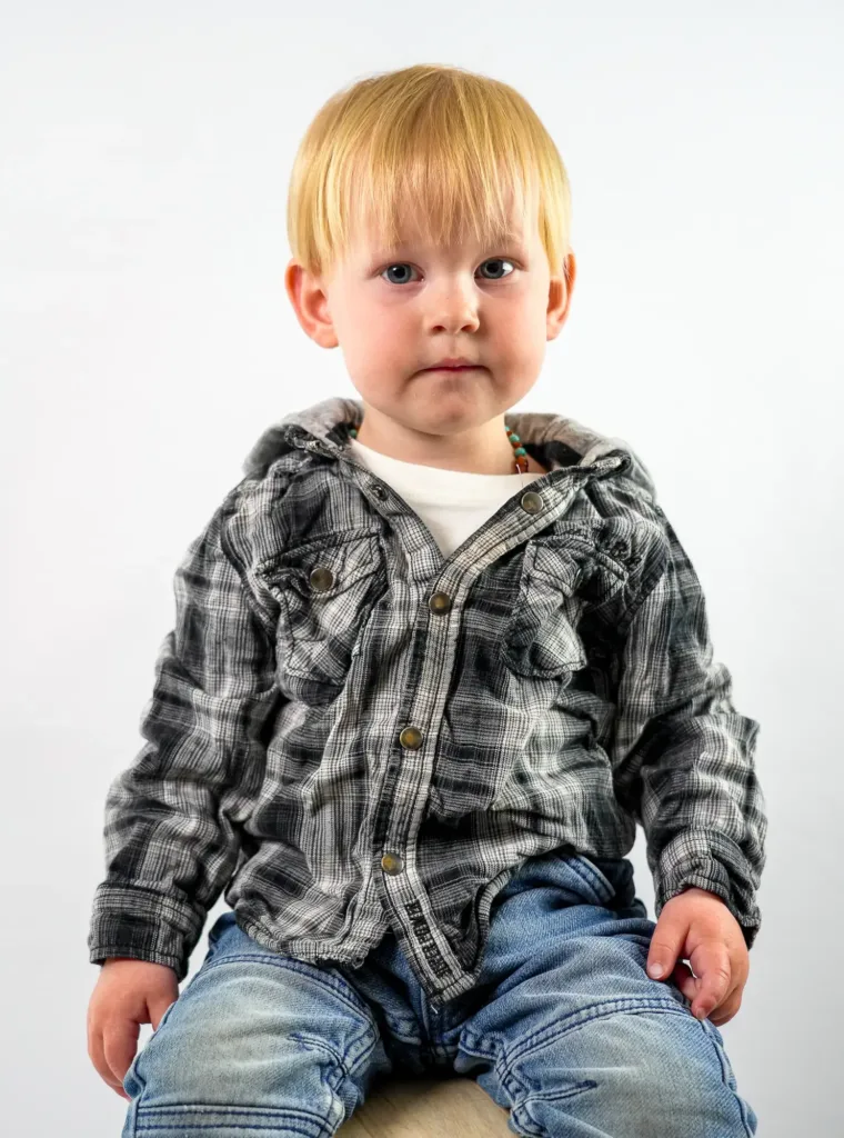 Photo d'un enfant de face, assis sur un tabouret, fond blanc en arrière-plan.