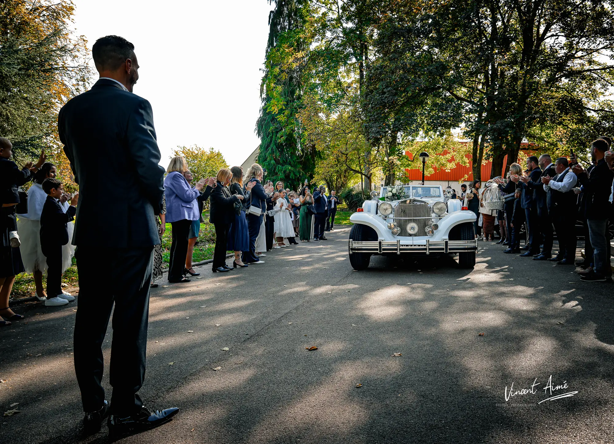 Le marié se tenant debout, face au cortège et à l'arrivée de la mariée dans une ancienne voiture blanche