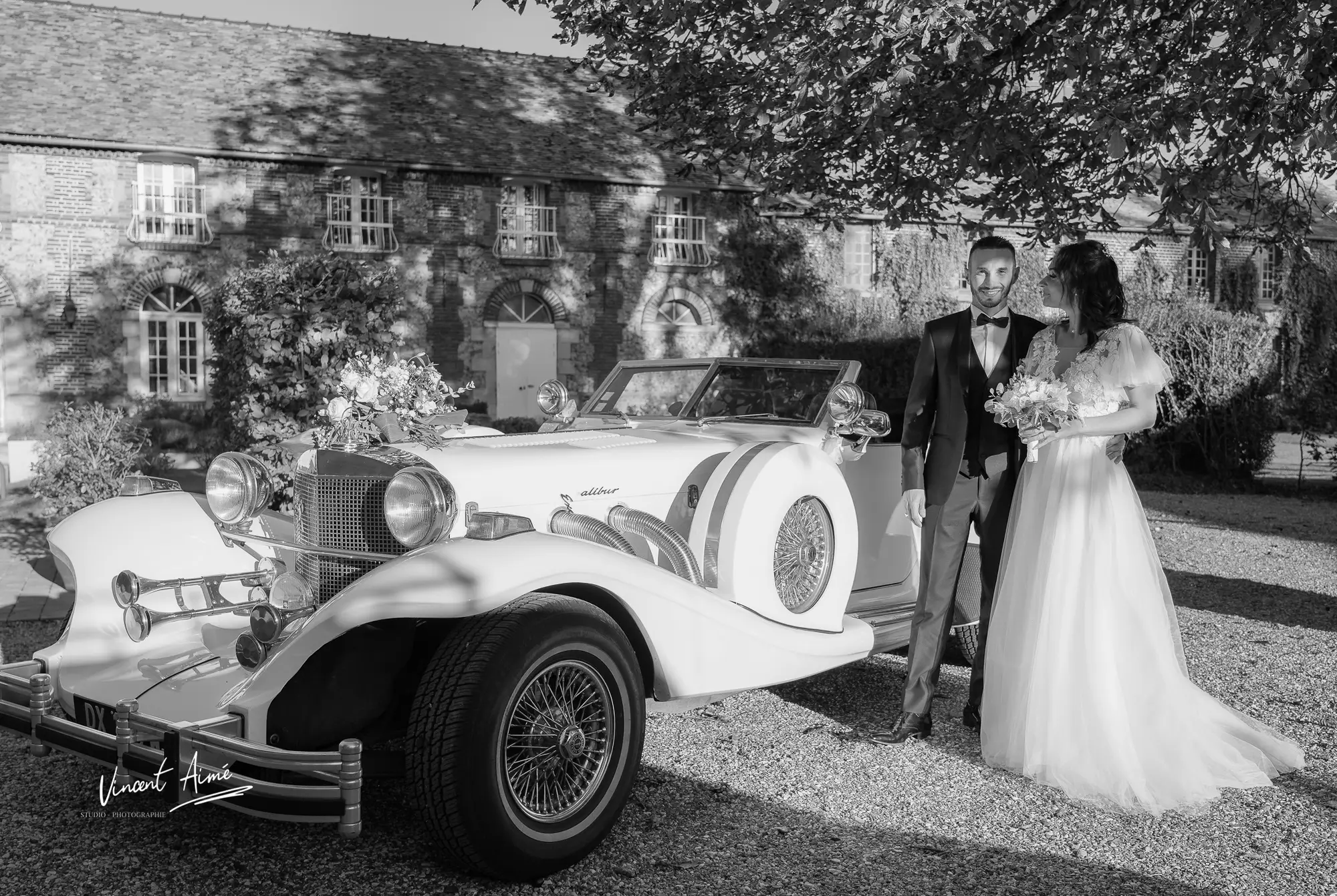 Les mariés posant devant leur voiture de mariage, photo en noir et blanc