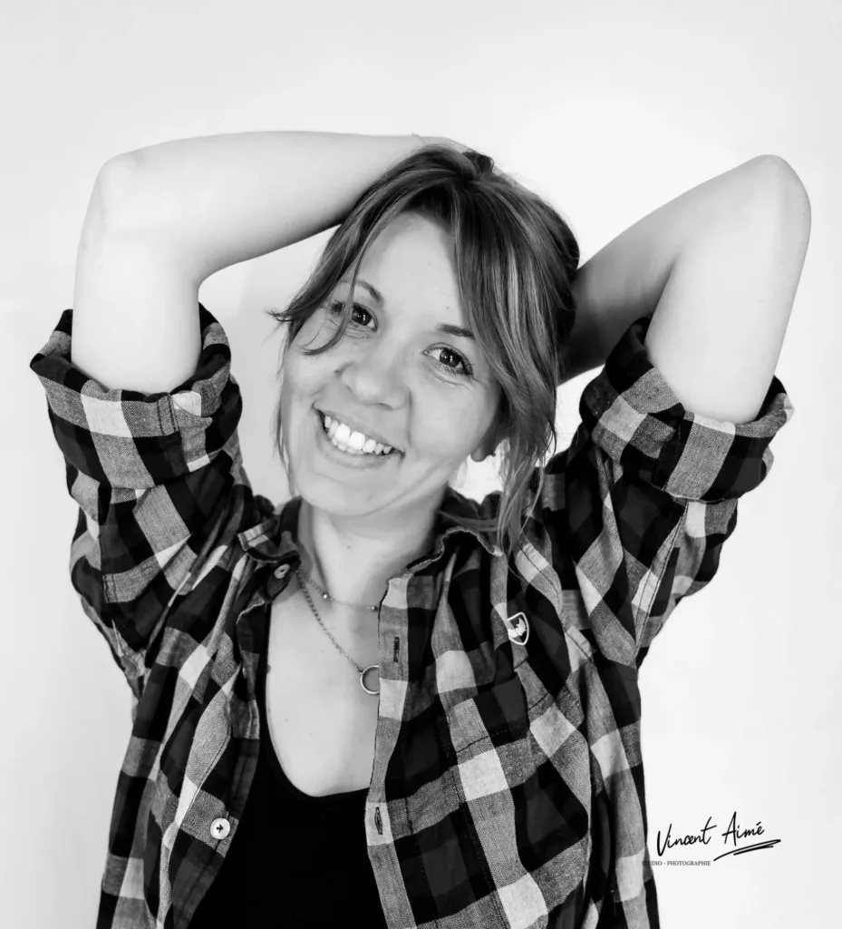 Portrait d'une femme en souriant avec les mains derrière la tête, portant une chemise à carreau. Photo en noir et blanc
