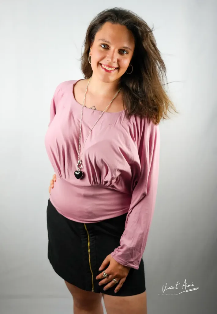 Portrait d'une femme se tenant debout, tout en sourire, haut rose et jupe noire.