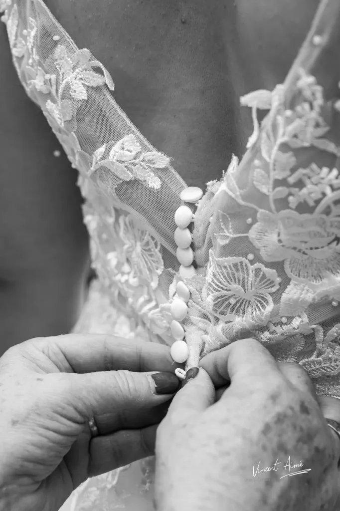 Main de la maman qui attache la robe de la mariée dans son dos
