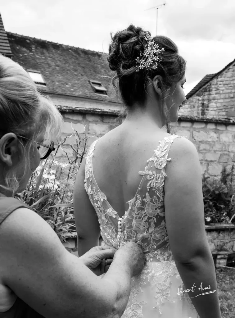 Main de la maman qui attache la robe de la mariée dans son dos