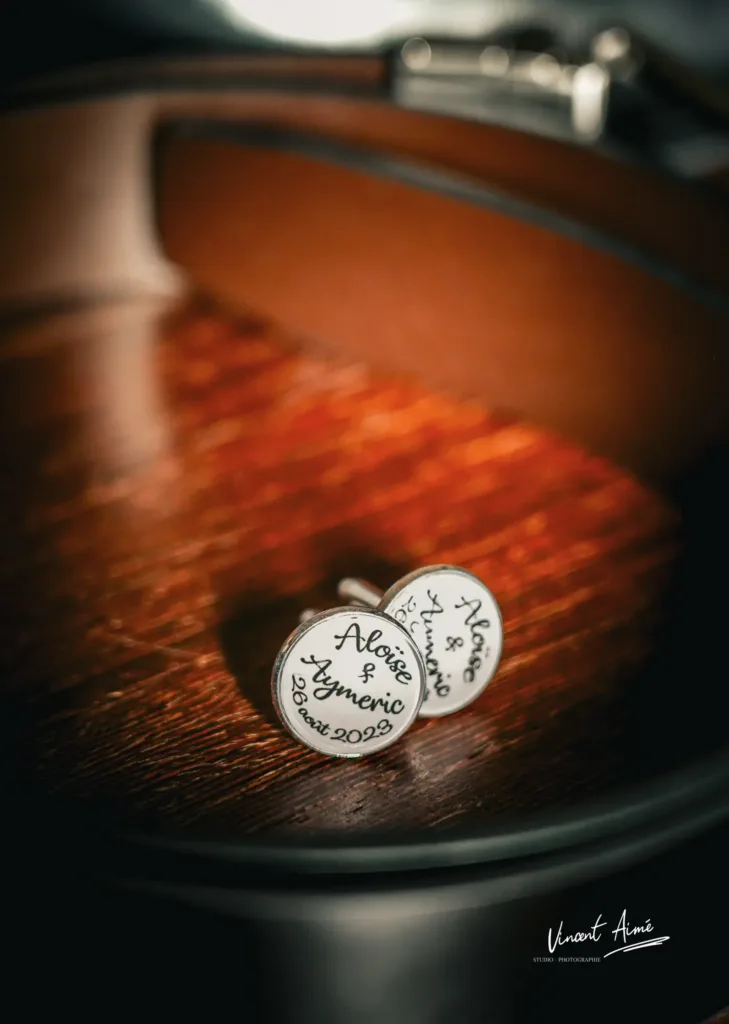 Boutons de manchettes posés sur une table en bois, indiquant les prénoms des mariés et la date du mariage